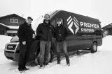 Three people stand next to a Premier Systems van in a snowy area.