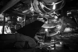A person working beneath large metallic equipment, likely repairing or inspecting it.