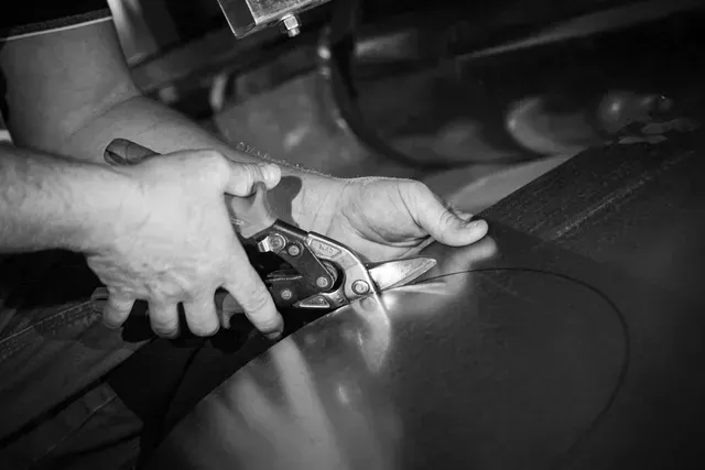 Person using metal shears to cut a curved line on a metal sheet.