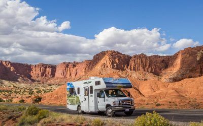 White camper van on a desert road with red cliffs and blue sky behind it