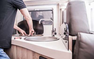 Person washing hands in a small sink inside a vehicle camper or RV.