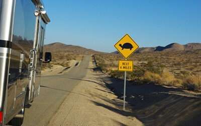 Desert road with a yellow warning sign showing a truck on a steep incline near a trailer