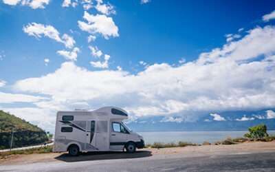 White camper van parked by a coastal road under a blue sky with clouds