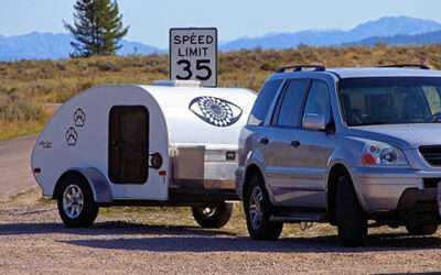 Silver SUV towing a white teardrop camper on a road near a speed limit 35 sign.