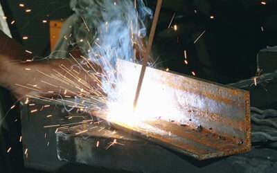 Welding sparks fly as a worker welds metal in a dark workshop.