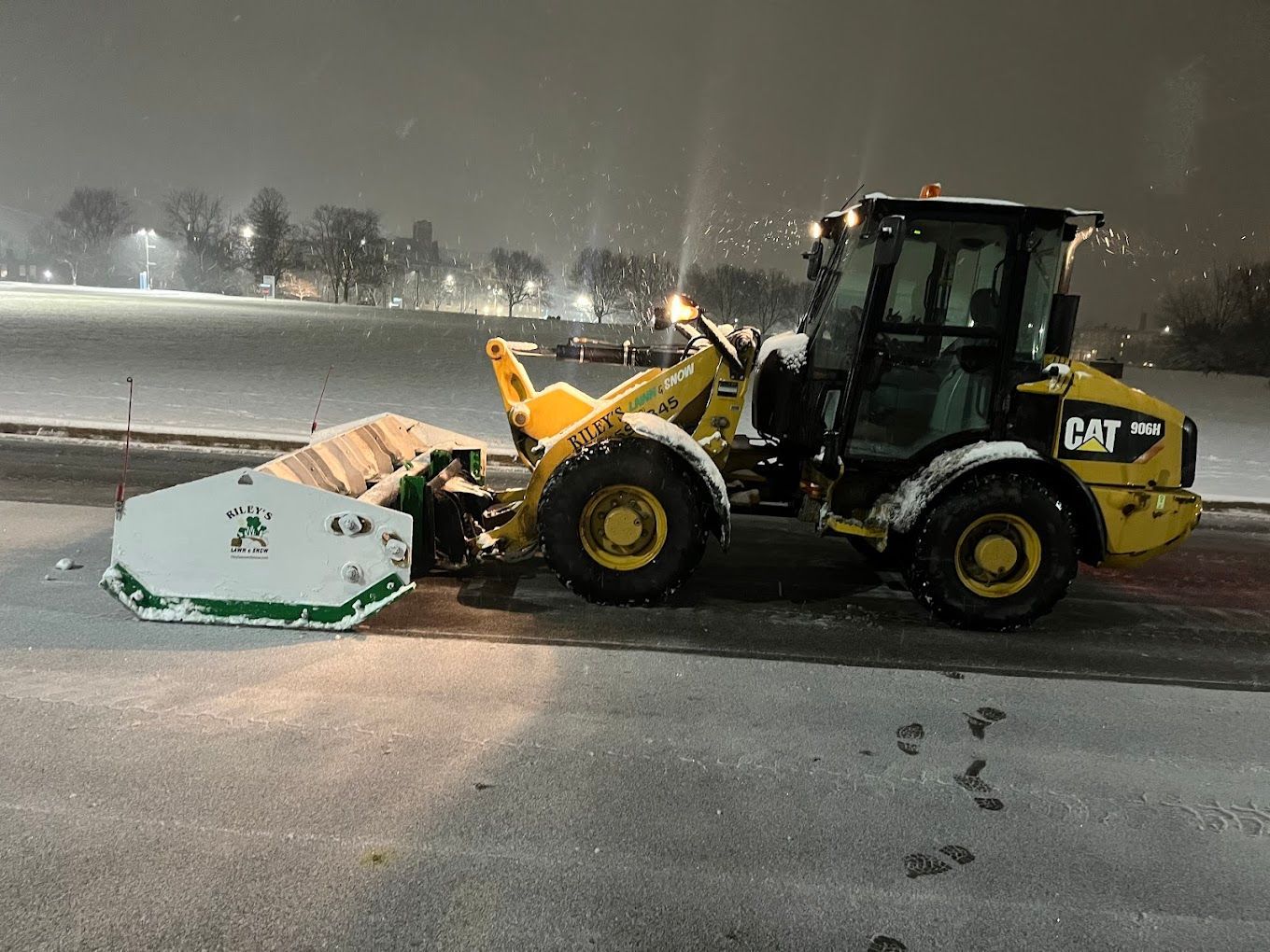 A yellow and black cat snow plow is parked on the side of the road at night.