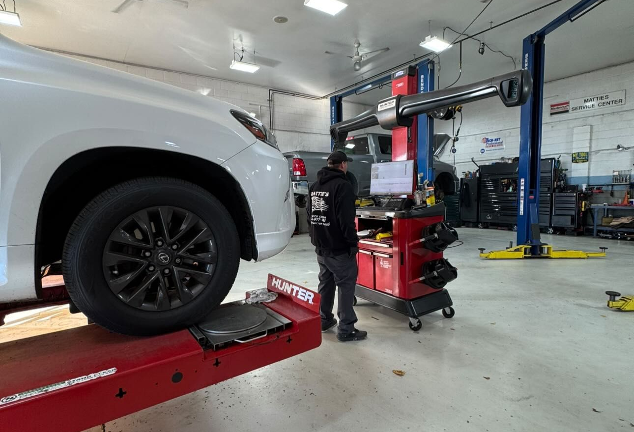 Mechanic aligning a white car's front tire in a garage, using alignment equipment.