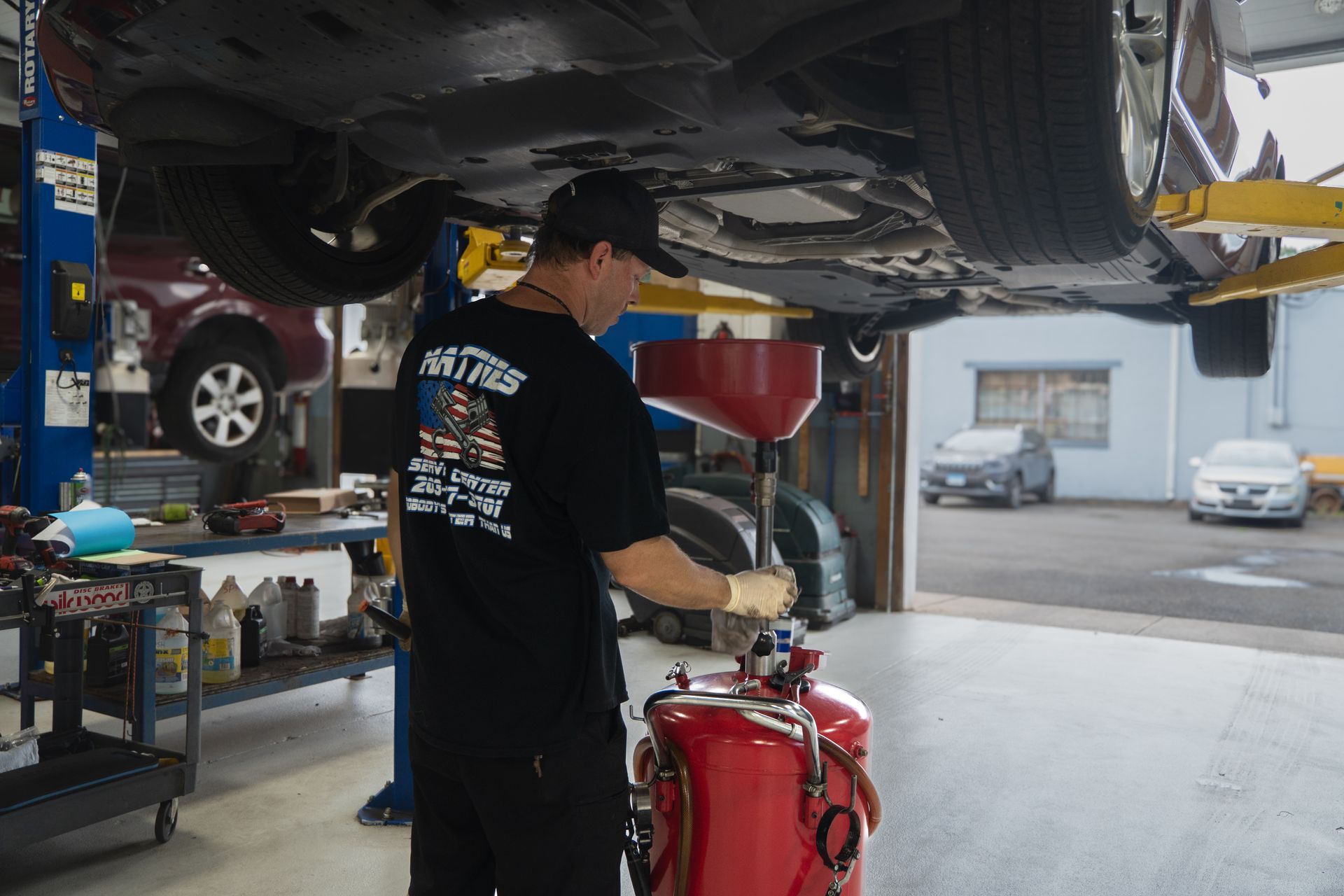 Mechanic draining oil from a car at a repair shop, using a red container to collect the oil.
