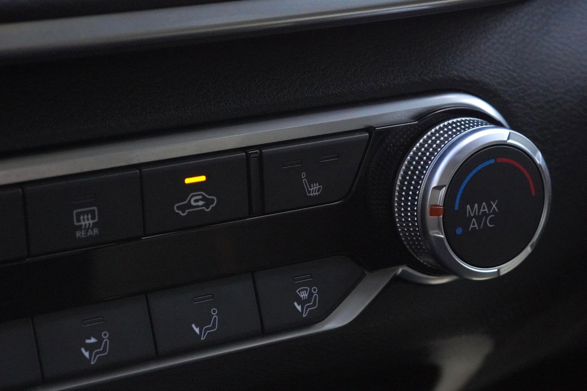 Car climate control panel: buttons, dial for temperature, lit vents icon.