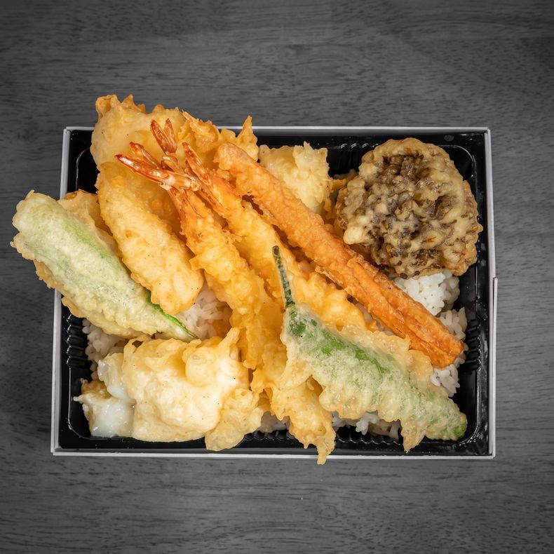 Assorted vegetable and shrimp tempura in a black bento box on a gray table