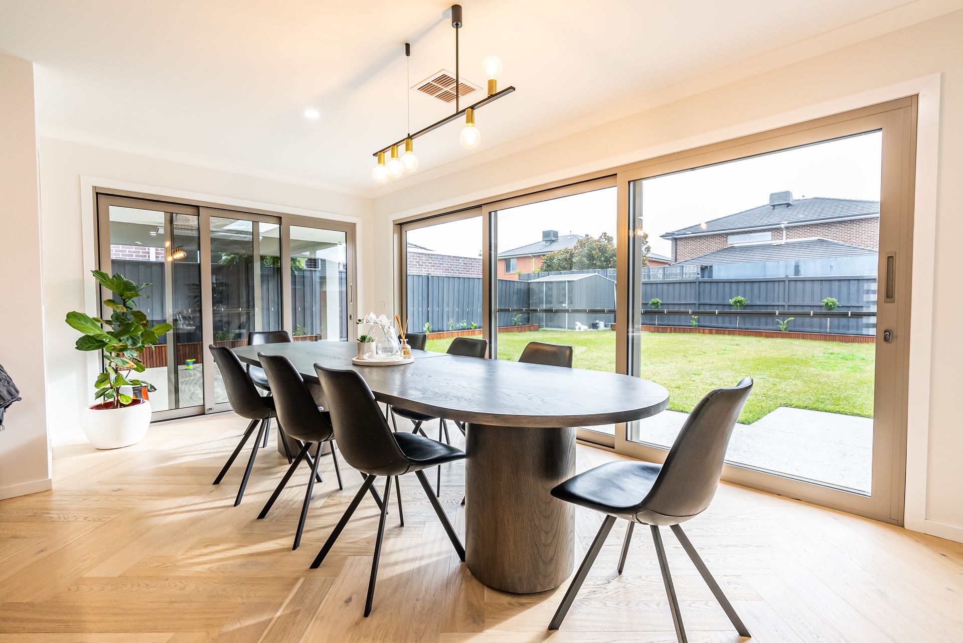 Bright dining room with oval table, black chairs, and large glass doors opening to a grassy backyard.