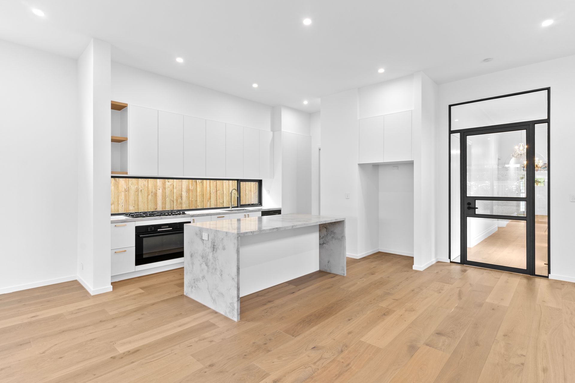Bright modern kitchen with white cabinets, marble island, wood floors, and black-framed glass door