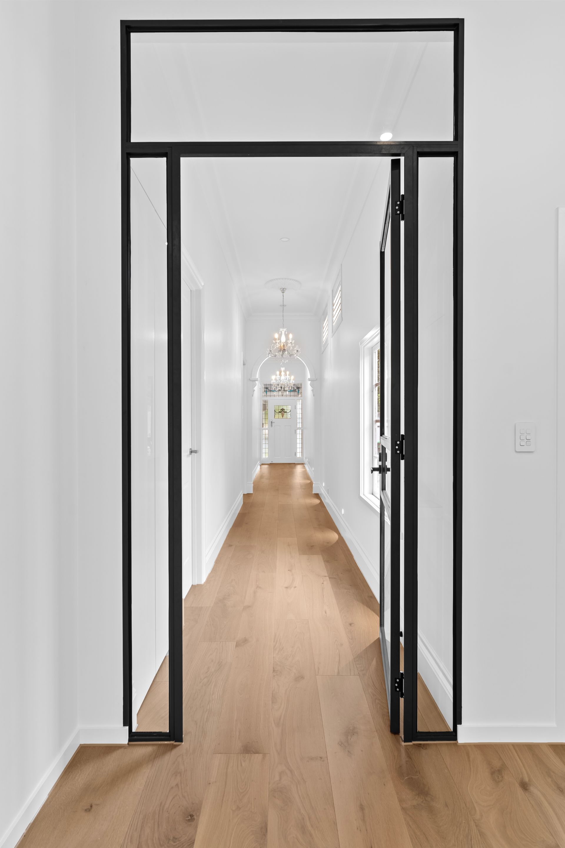 Narrow white hallway with a wooden floor and a black-trimmed doorway in the foreground