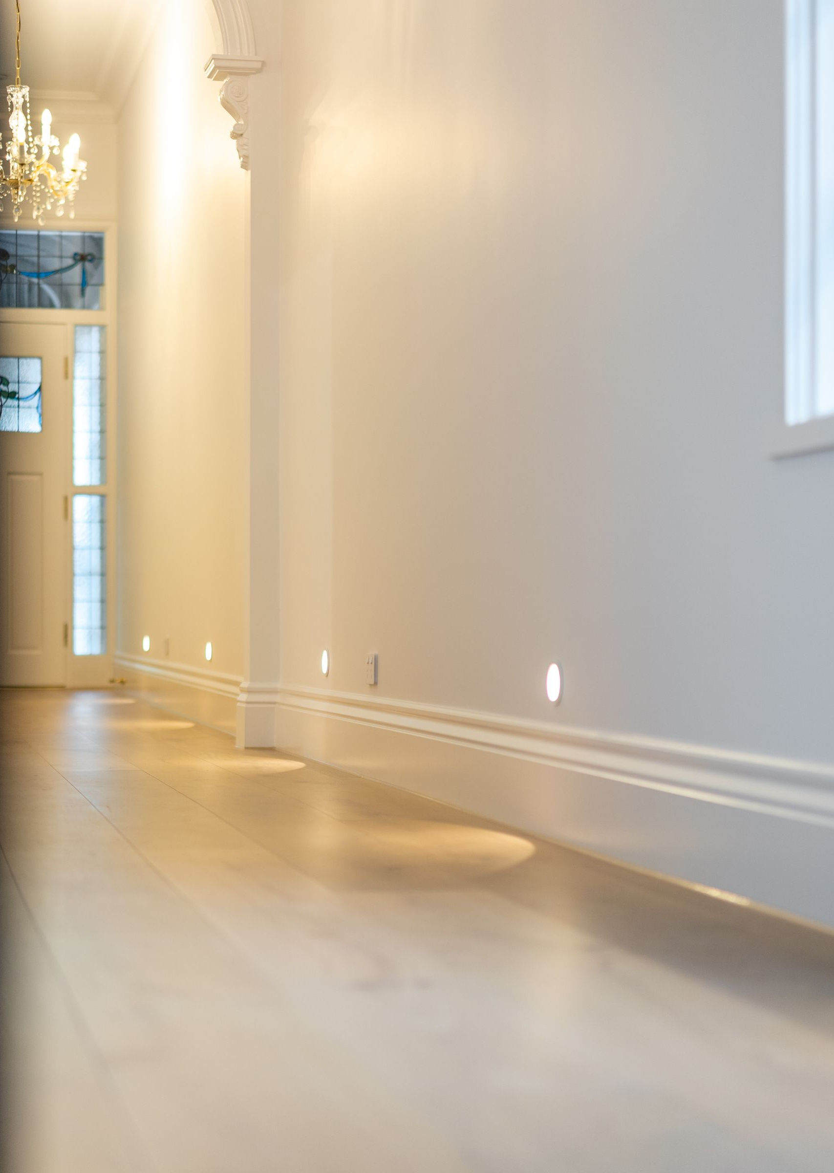 Empty sunlit hallway with white walls, wooden floor, and soft shadows