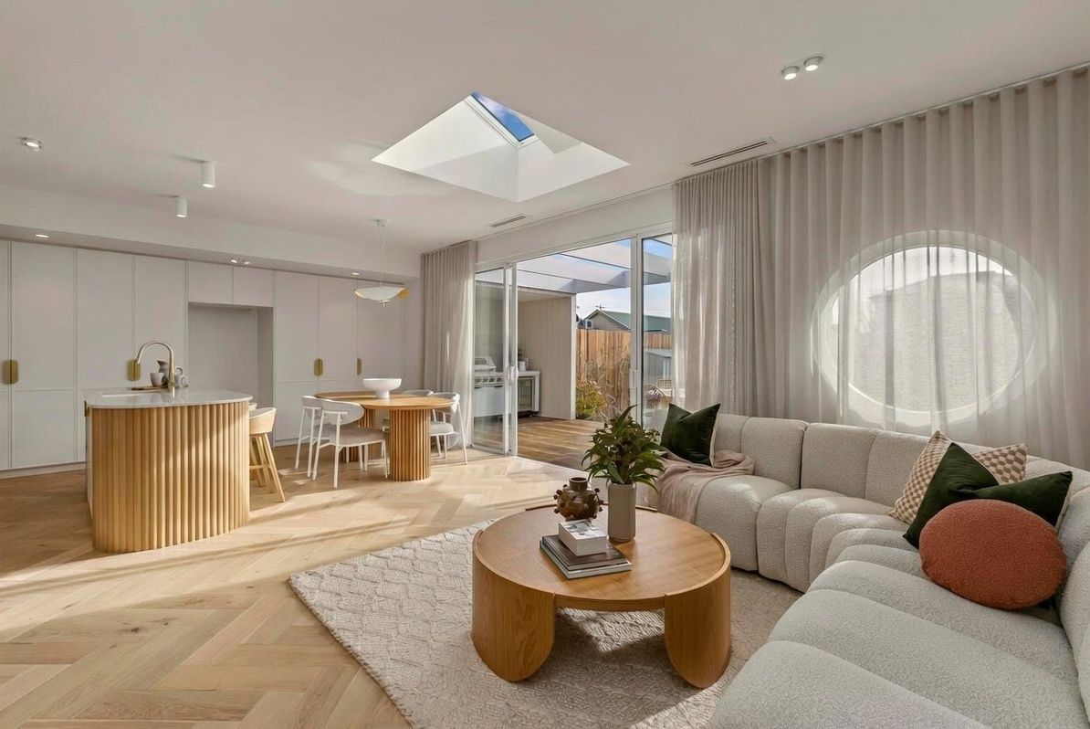 Bright modern living room with a sectional sofa, round coffee table, and open kitchen in warm neutral tones