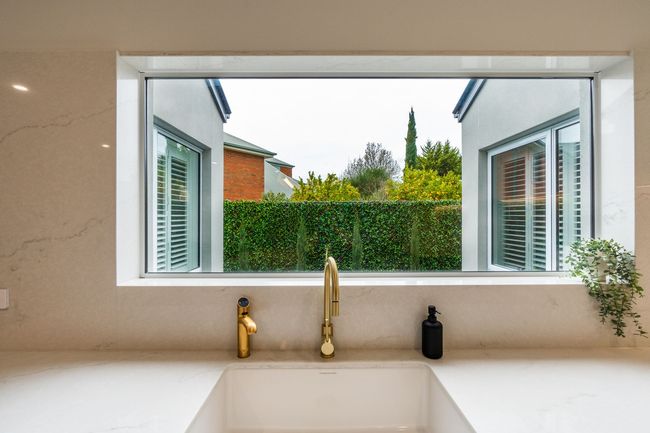 Modern kitchen sink beneath a wide window, overlooking a garden and neighboring houses