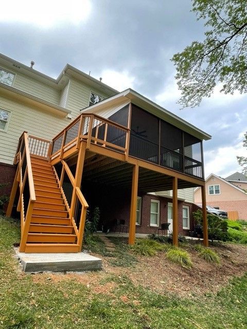 A screened in deck with stairs leading up to it and a house in the background.