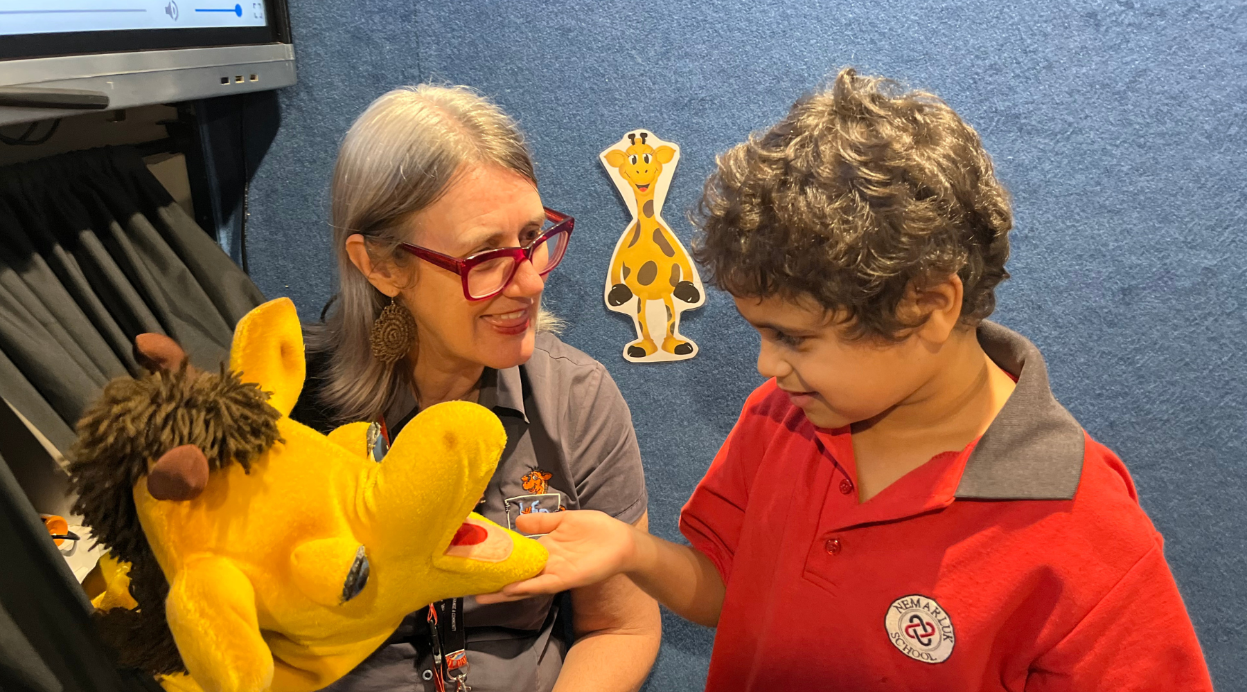 A woman is holding a stuffed animal next to a boy in a red shirt.