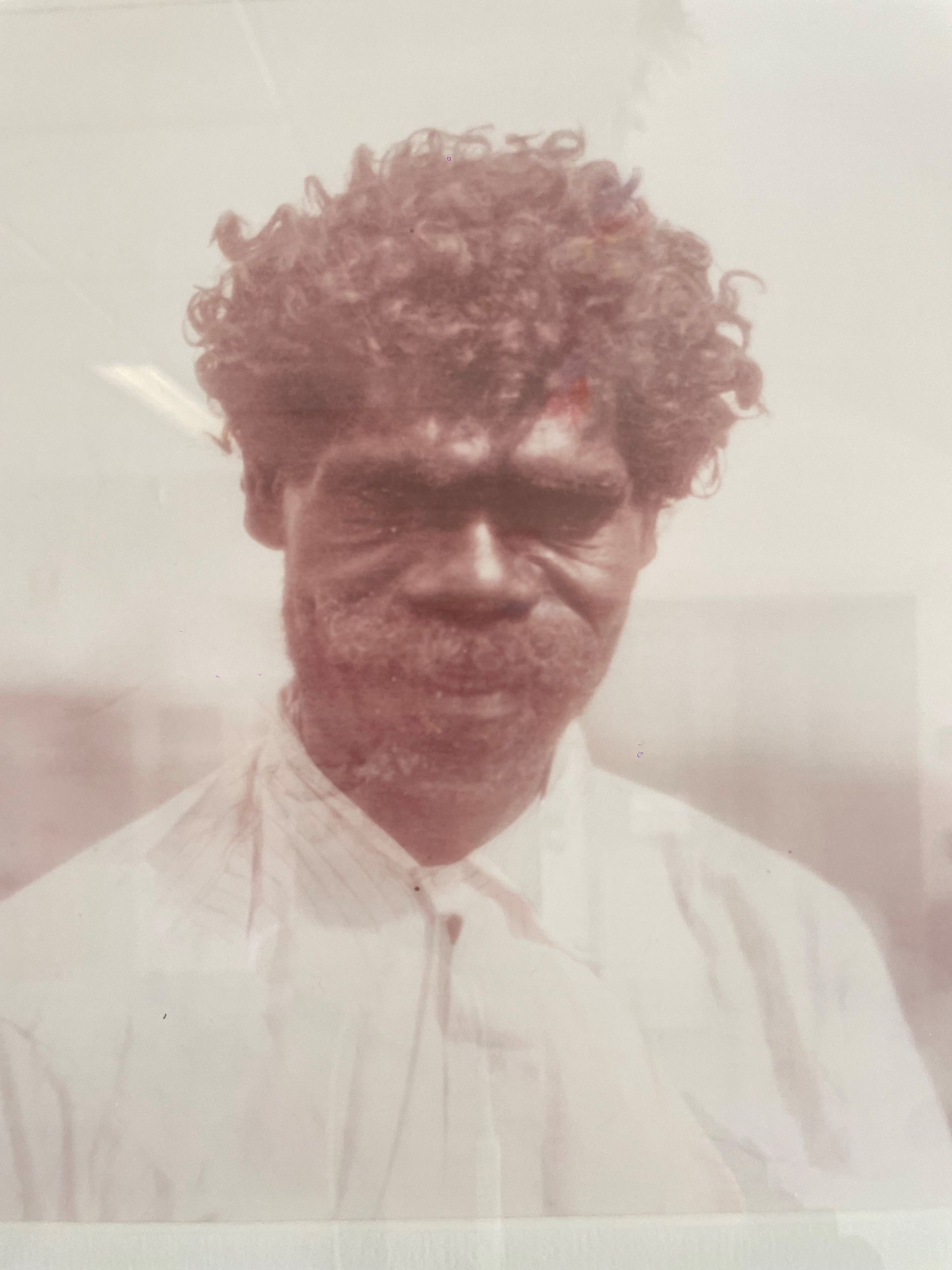 A man with curly hair and a beard is wearing a white shirt and tie.
