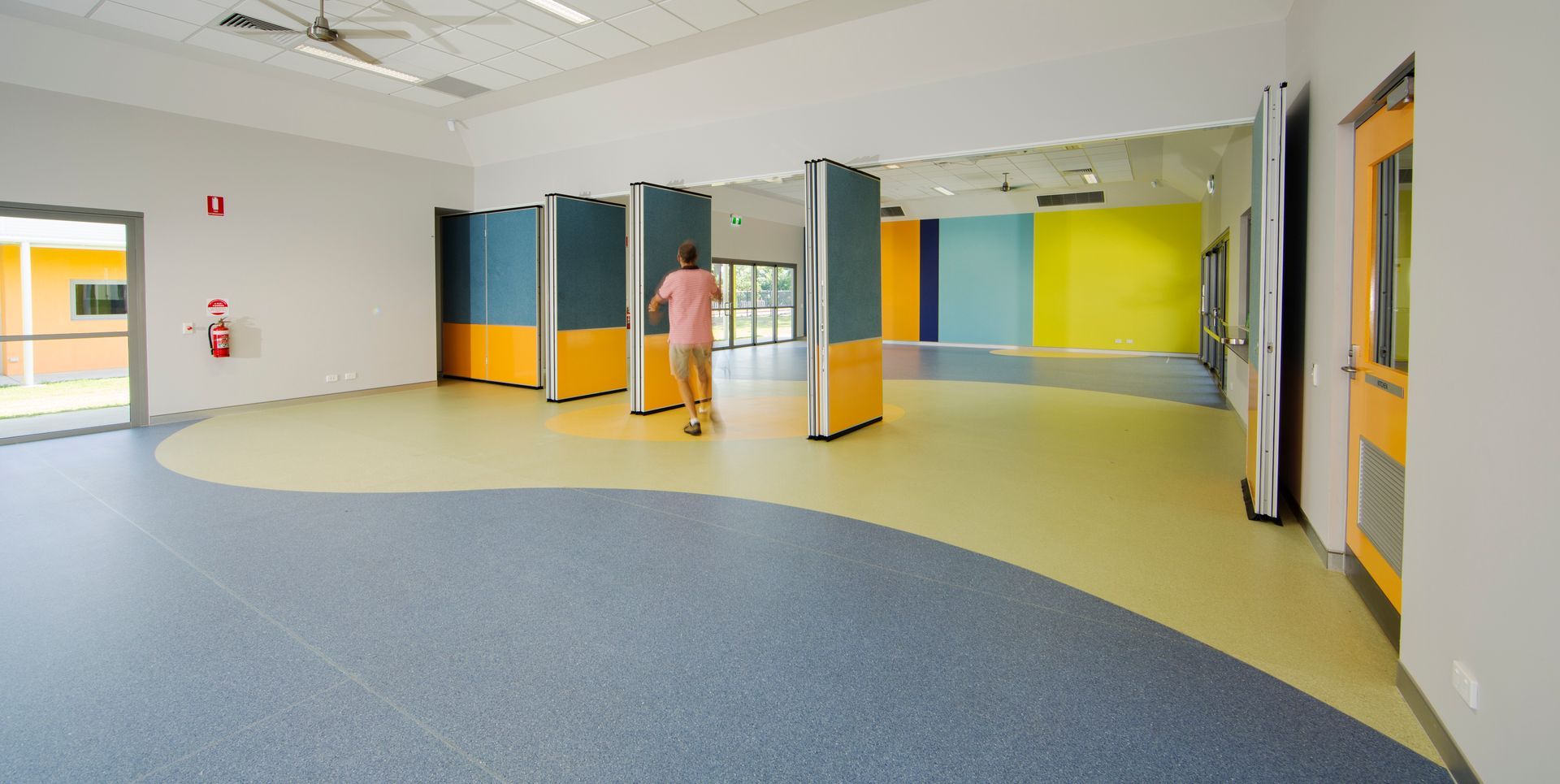 A person is standing in a large room with a blue and yellow carpet.