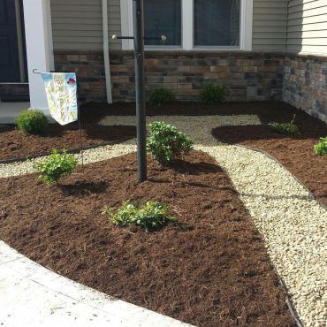 Landscaped front yard with mulch beds, stone paths, bushes, and flag.