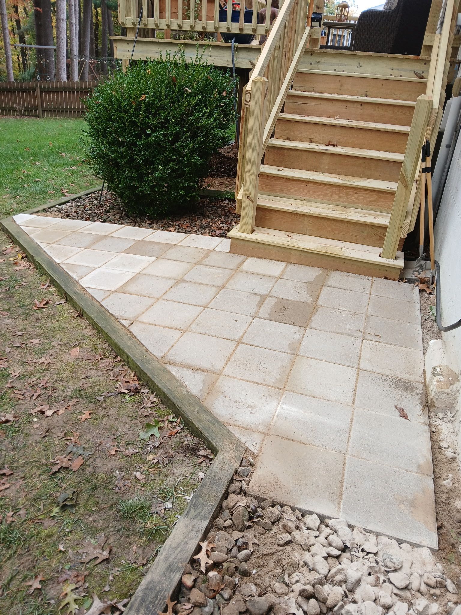 Stone pathway leading to wooden stairs, bordered by wooden beam and soil, in a backyard setting.