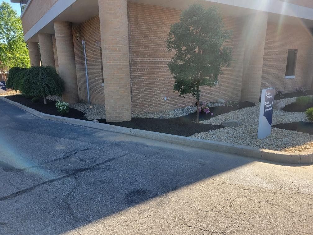 Building exterior with landscaping, asphalt road, mulch, trees, and sign.