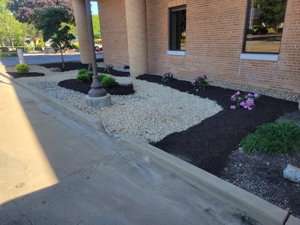Landscaped area with beige gravel and dark mulch. Building with brick facade.