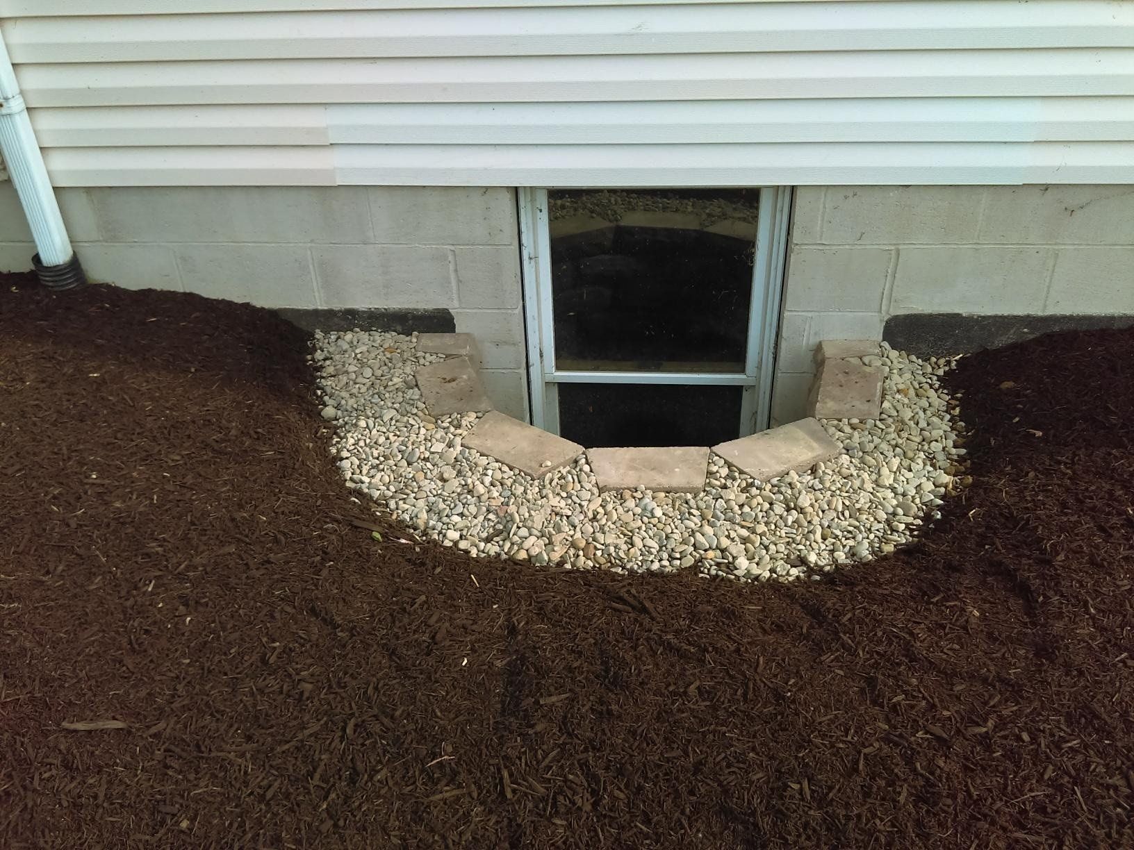 Window well with gravel and mulch next to a building's foundation.