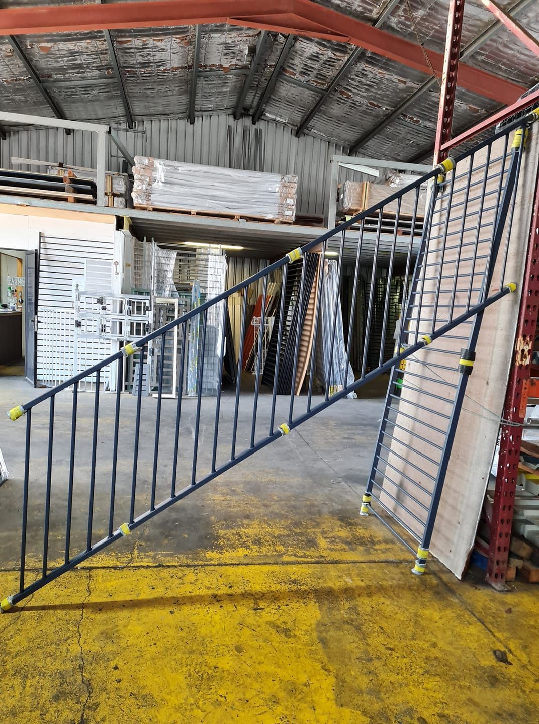 A Black Metal Staircase Railing Leans Against a Wall in a Warehouse — Metal Fencing Supplies In Harrington, NSW