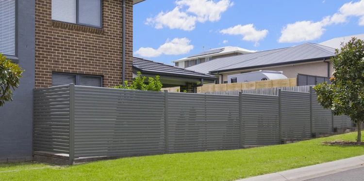 Gray Slatted Fence in Front of Brick House and Green Lawn Under a Blue Sky — Metal Fencing Supplies In Forster, NSW