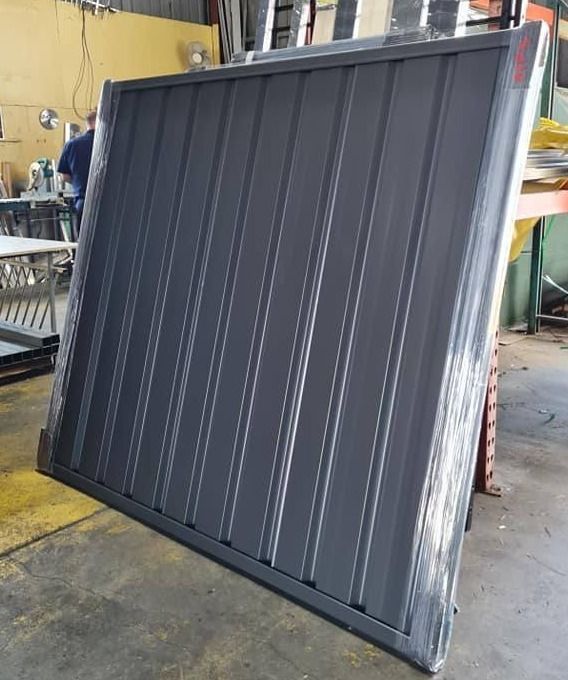 A Gray Metal Fence Panel Stands Against a Warehouse — Metal Fencing Supplies In Taree, NSW
