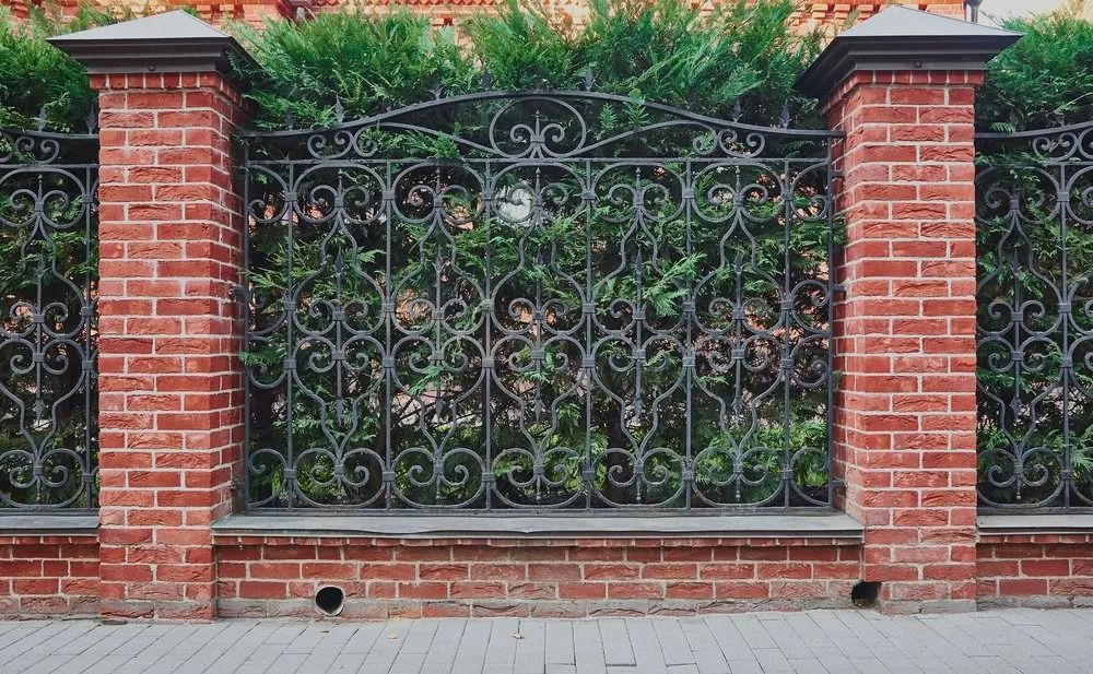 Brick Pillars With an Ornate Iron Fence and Green Shrubbery — Metal Fencing Supplies In Taree, NSW