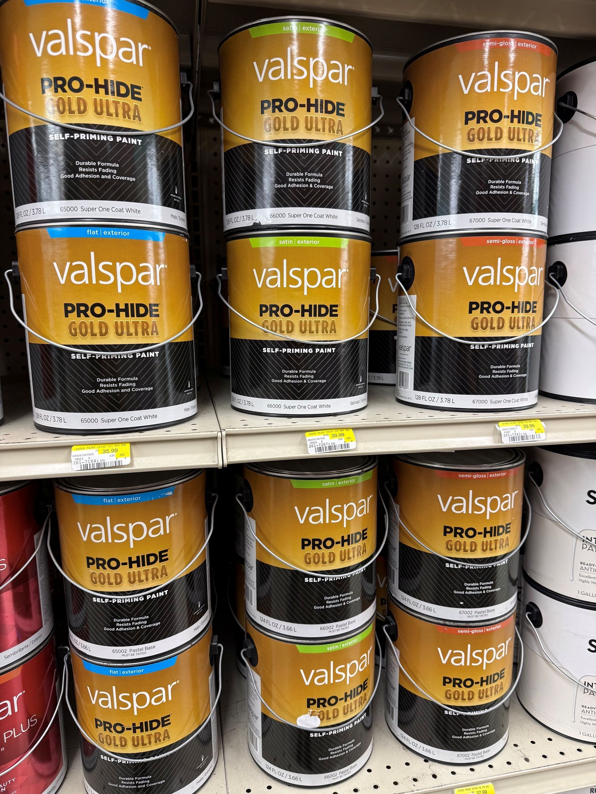 Shelves of stacked Valspar Pro-Hide paint cans in gold, black, and red labels at a store.