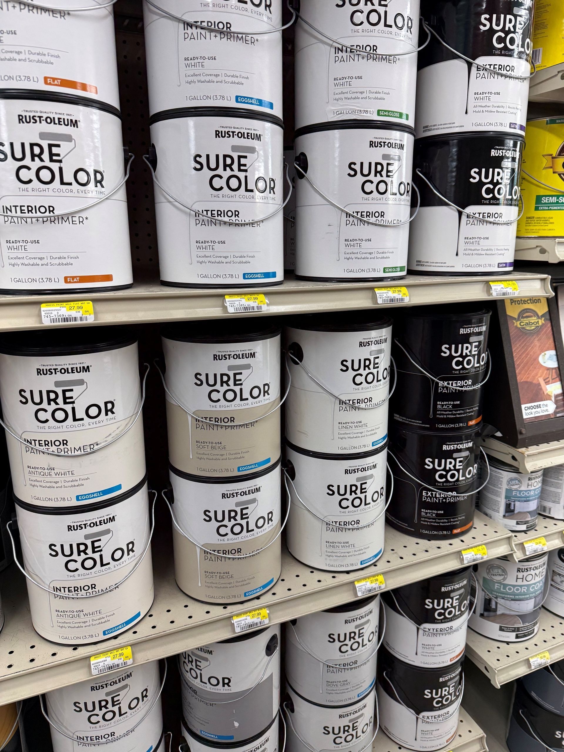Paint cans stacked on store shelves, mostly white and black labels in a paint aisle.
