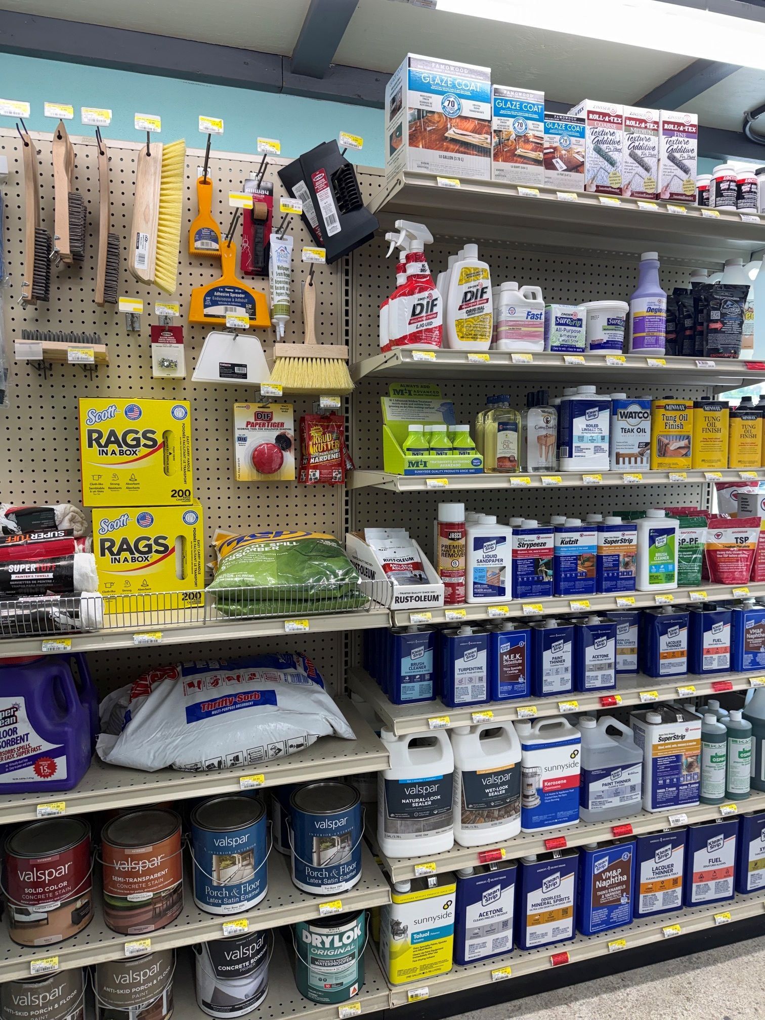 Hardware store aisle with shelves of tools, adhesives, and caulk in assorted colors.