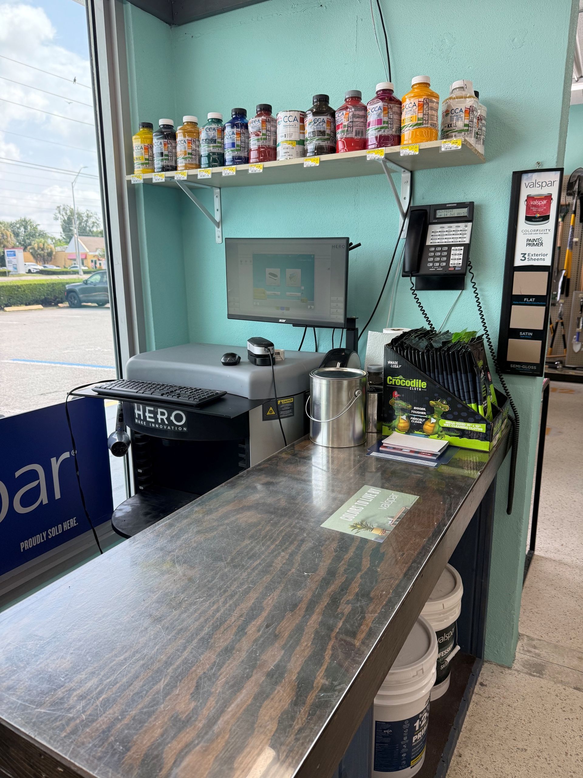 Small beverage counter with syrups on shelves, coffee machine, and cups beneath a window.