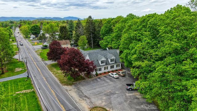 Residential setting aerial view of a house on the side of a road, surrounded by trees.