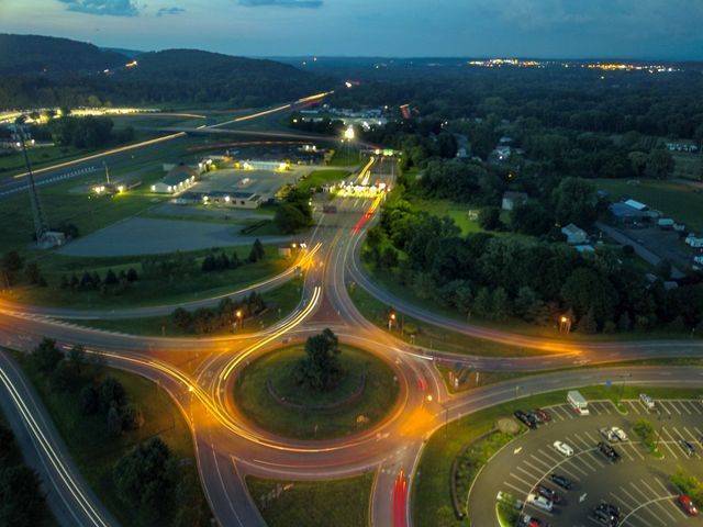 An aerial view of a roundabout at night with a parking lot in the foreground.