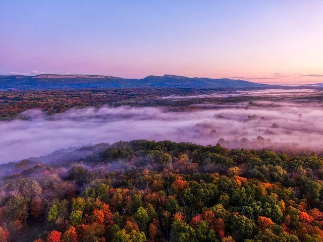 Aerial view foggy forest photography by Hudson Valley Drones, capturing a scenic sunset over mountains in the background.