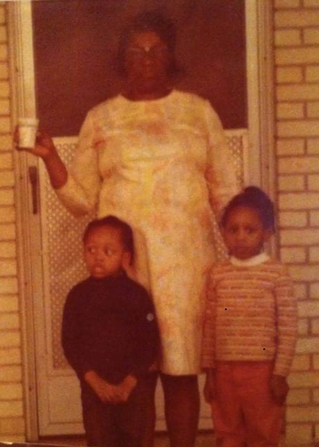 Woman and two children pose in front of a door. The woman holds a cup.