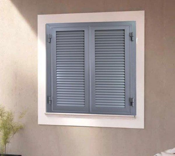 Persiane grigie a lamelle incastonate in una cornice bianca su una parete beige