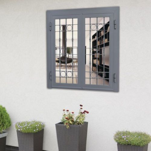 Finestra grigia con sbarre metalliche sopra tre piante in vaso, sullo sfondo di una parete esterna bianca.