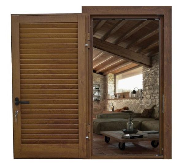 Porta a persiana in legno parzialmente aperta su un soggiorno rustico con pareti in pietra e divano.