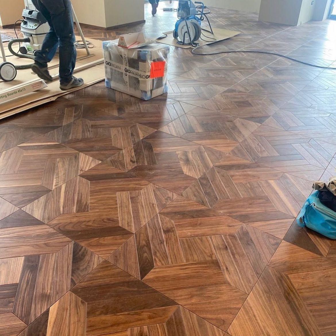Operai intenti a rifinire un pavimento in legno a spina di pesce con attrezzi e attrezzature in una stanza in fase di ristrutturazione.