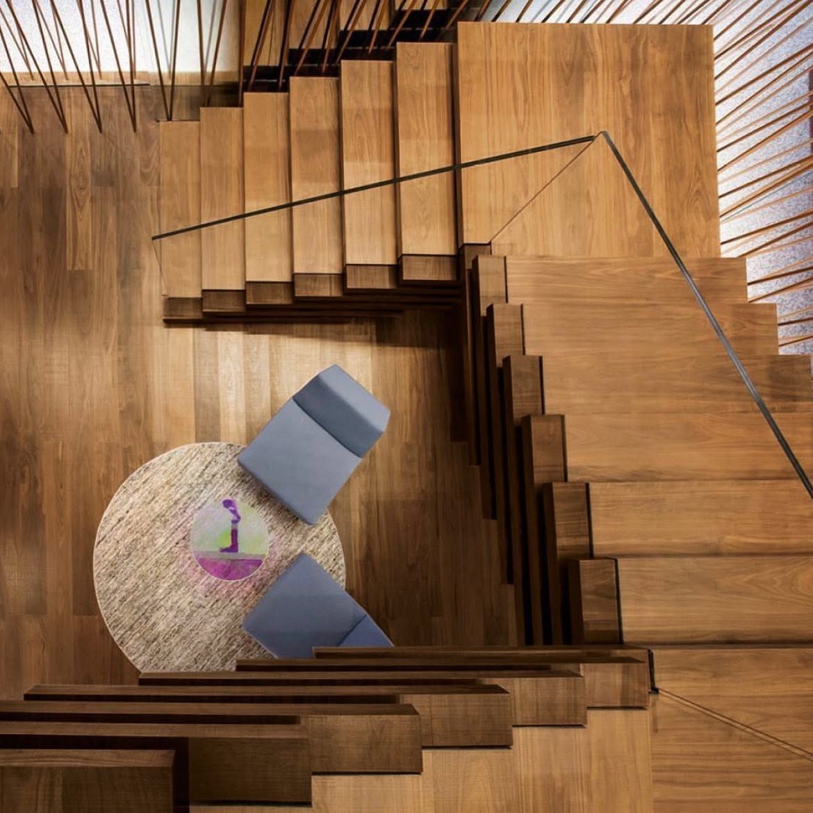Vista dall'alto di una moderna scala in legno con un tappeto rotondo e due sedie blu attorno a un piccolo oggetto viola