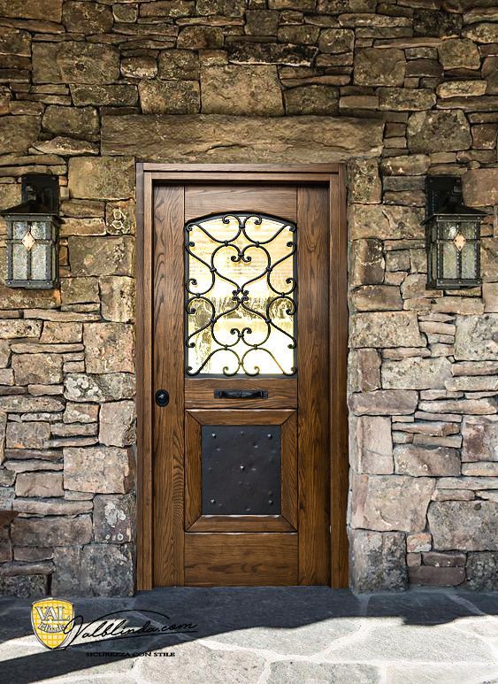 Porta d'ingresso in legno con pannello in vetro e ferro battuto in un muro di pietra, fiancheggiata da due lanterne