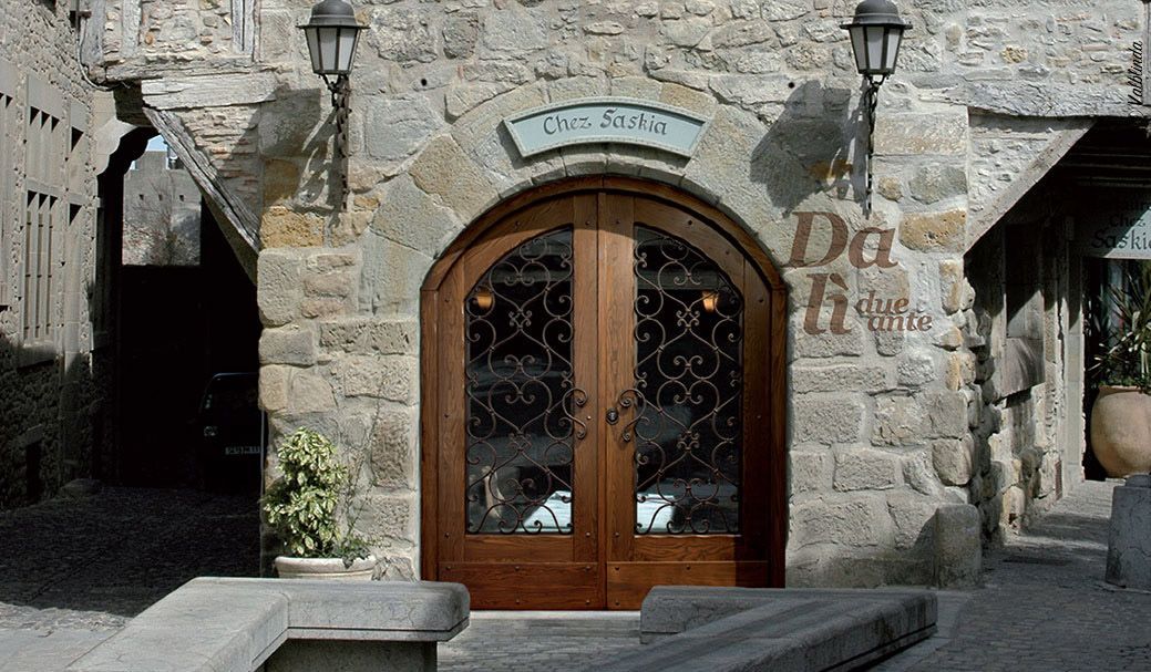Ingresso di un edificio in pietra con doppie porte ad arco in legno e lanterne, incorniciate da piante in vaso.