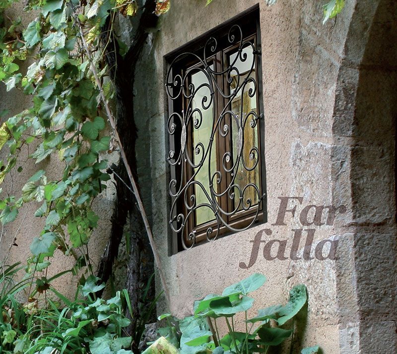 Muro in pietra ricoperto di edera e grata decorativa in ferro battuto accanto a un arco.