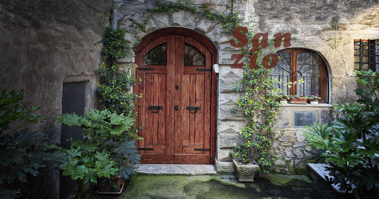 Ingresso di un cottage in pietra con porta ad arco in legno, finestra e muri ricoperti di edera.